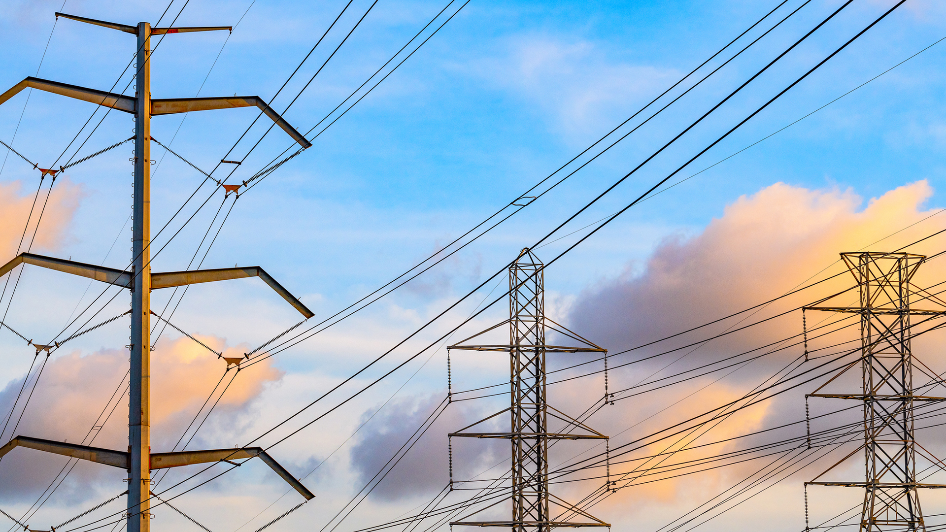 High-voltage transmission lines poles against a blue sky with clouds